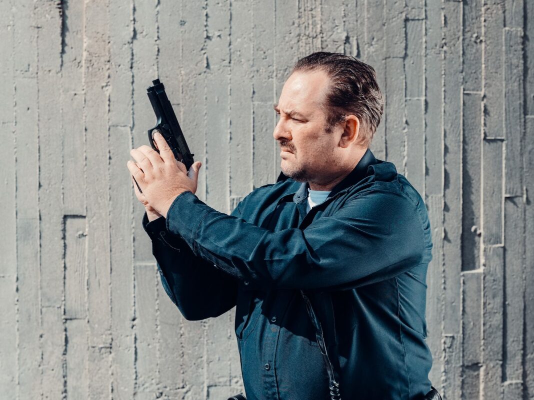 Policjant przy betonowej ścianie zabezpiecza broń palną Policjant przy betonowej ścianie zabezpiecza broń palną