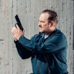 Symulatory strzeleckie w policji i wojsku: czy wirtualne strzelanie może zastąpić klasyczną strzelnicę w procesie szkolenia funkcjonariuszy Policjant przy betonowej ścianie zabezpiecza broń palną