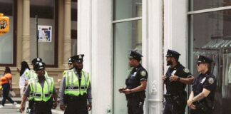 Funkcjonariusze NYPD w mundurach patrolują ruchliwą ulicę w ciągu dnia