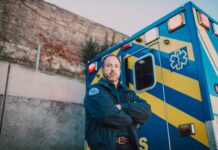 Ratownik medyczny stoi obok niebiesko-żółtej karetki na zewnątrz