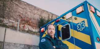 Ratownik medyczny stoi obok niebiesko-żółtej karetki na zewnątrz